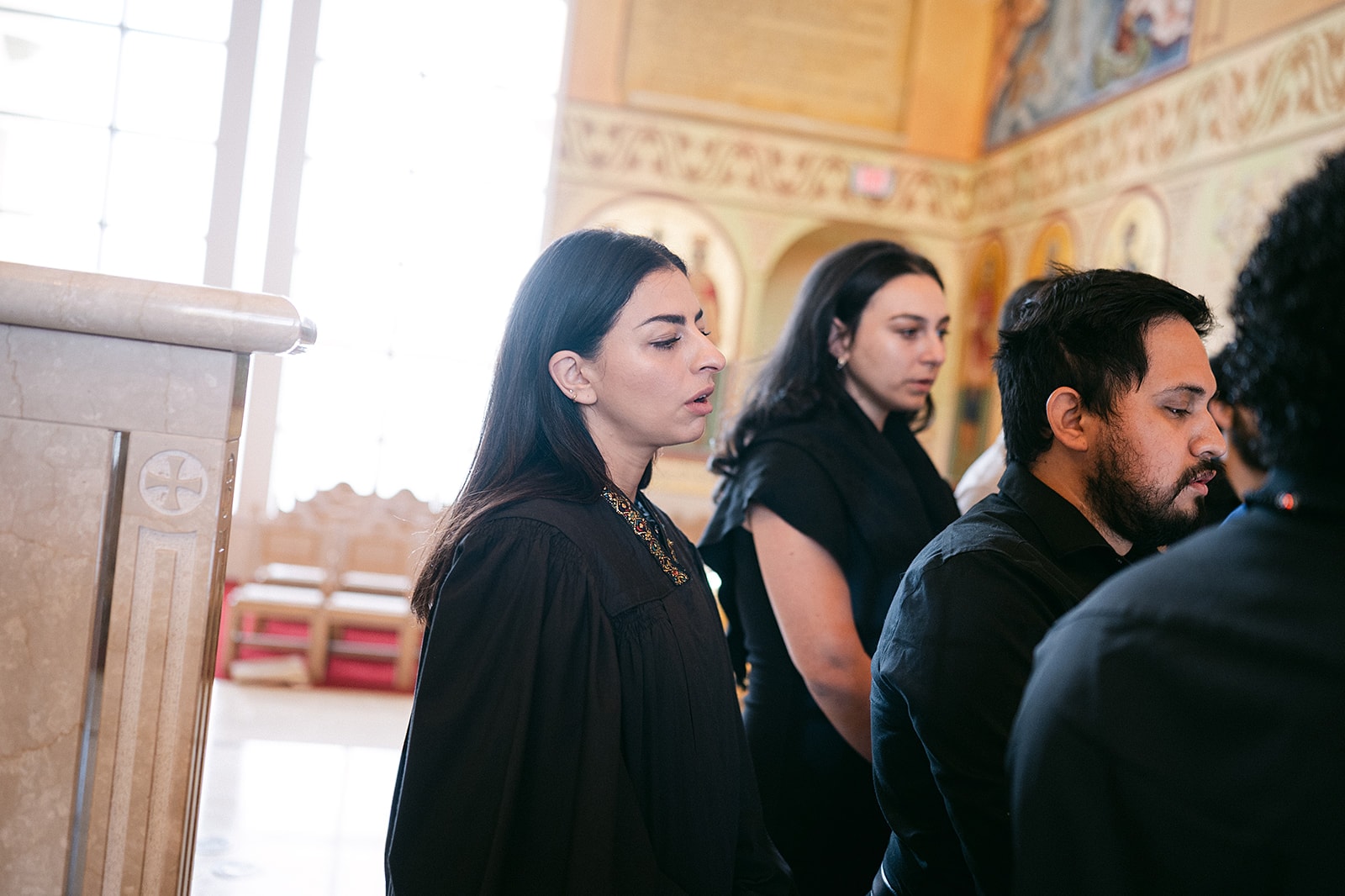 Participants in black robes chanting side by side during the Liturgy